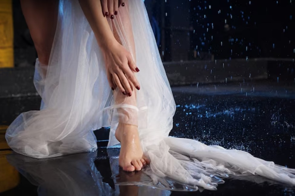 a photo of a female in a white long dress washing her feet in the water with splashes