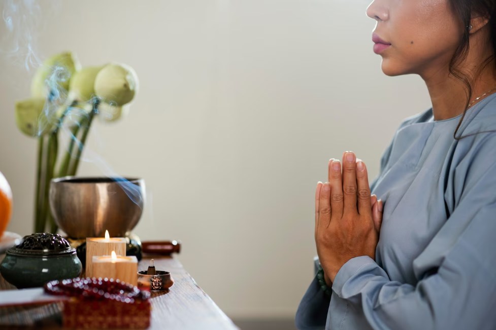 a side view of a woman praying in front of the candles