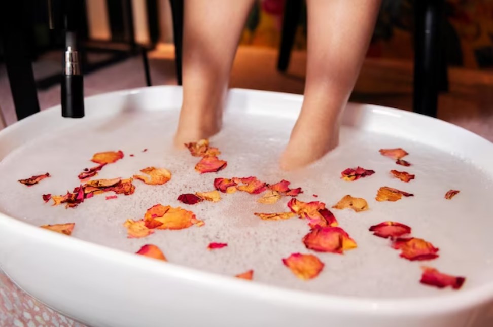 female feet put in a bucket with petals for a pedicure